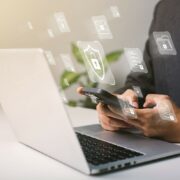 Illustration of password reuse. Person holding cell phone in front of open laptop with transparent security icons floating around